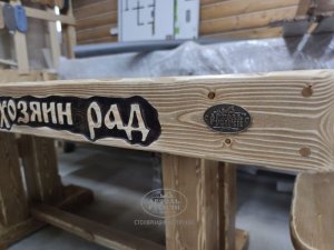 Фирменный знак Артель Русичи из латуни на добротном деревянном столе с резной надписью в русском стиле